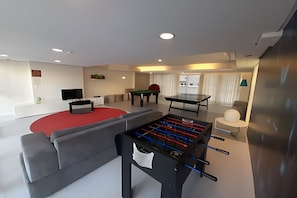 A modern living room with a foosball table, a pool table, and a flat-screen TV. - SHB Alto padrão com Vista Panorâmica (Santos)