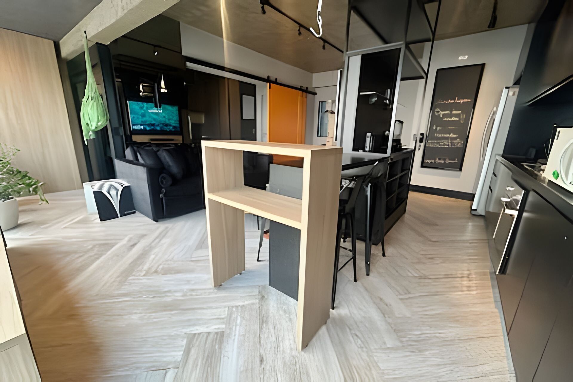 Una cocina moderna con encimera de madera, una zona de comedor con mesa y sillas negras, y una sala de estar con sofá y televisor.