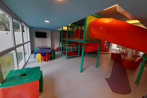 Ein Kinderspielbereich mit Rutsche, Klettergerüsten und bunten Sitzgelegenheiten.
