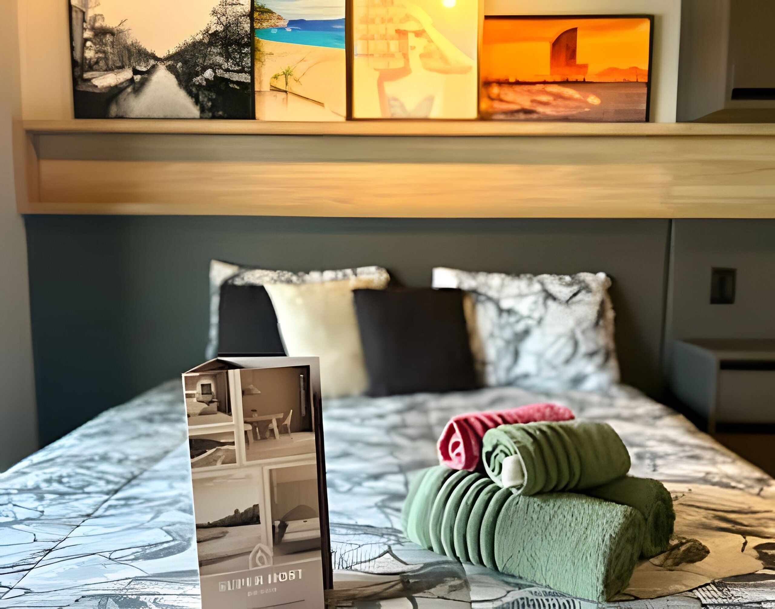 Una habitación de hotel con una cama, almohadas, una toalla doblada con cuidado y un folleto sobre la cama.