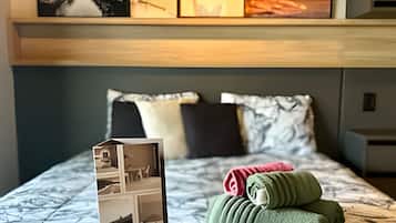 Una habitación de hotel con una cama, almohadas, una toalla doblada con cuidado y un folleto sobre la cama.