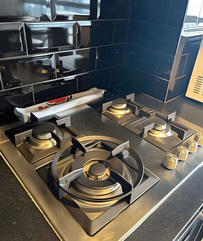 A modern kitchen with four gas burners, stainless steel appliances, and a black tiled backsplash. - SHB Alto padrão com Vista Panorâmica (Santos)