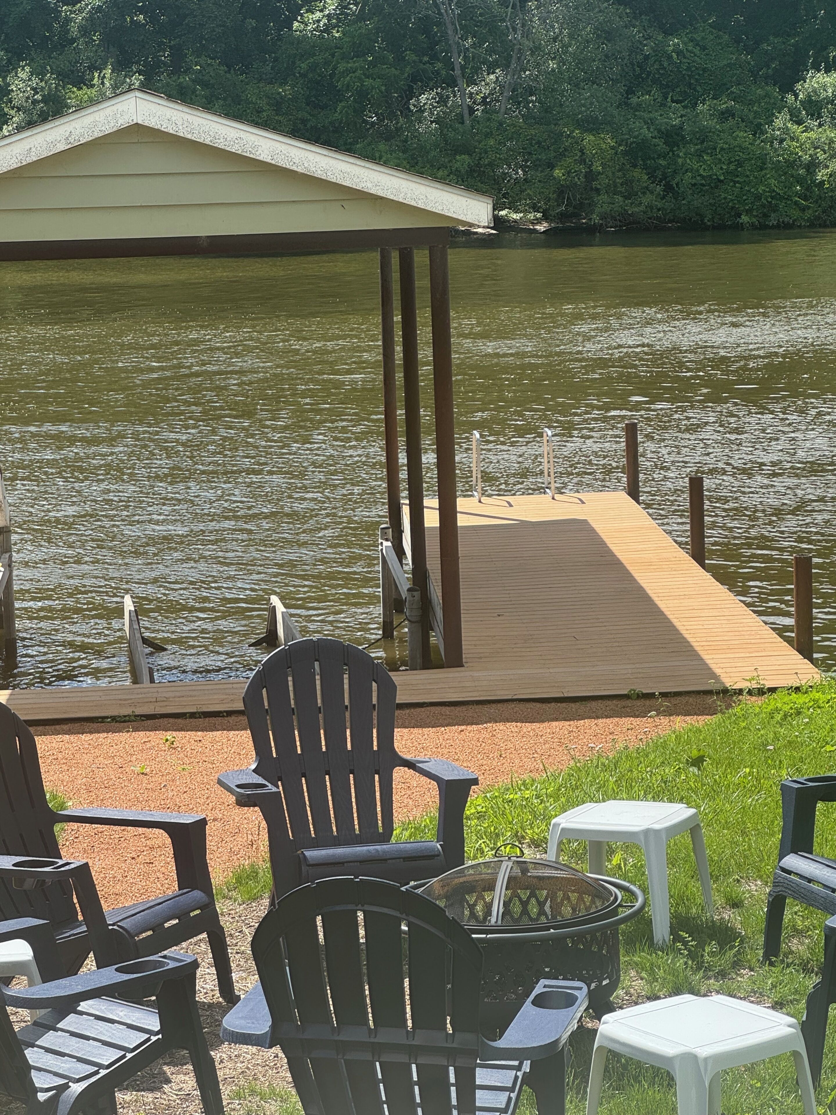 Une terrasse au bord du lac, avec des chaises et une table, une jetée en bois s’avançant dans l’eau et, au fond, une zone abritée.