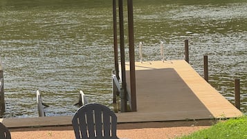 En træterrasse ved søen med stole og et bord, en træbro der strækker sig ud i vandet, og et overdækket område i baggrunden.