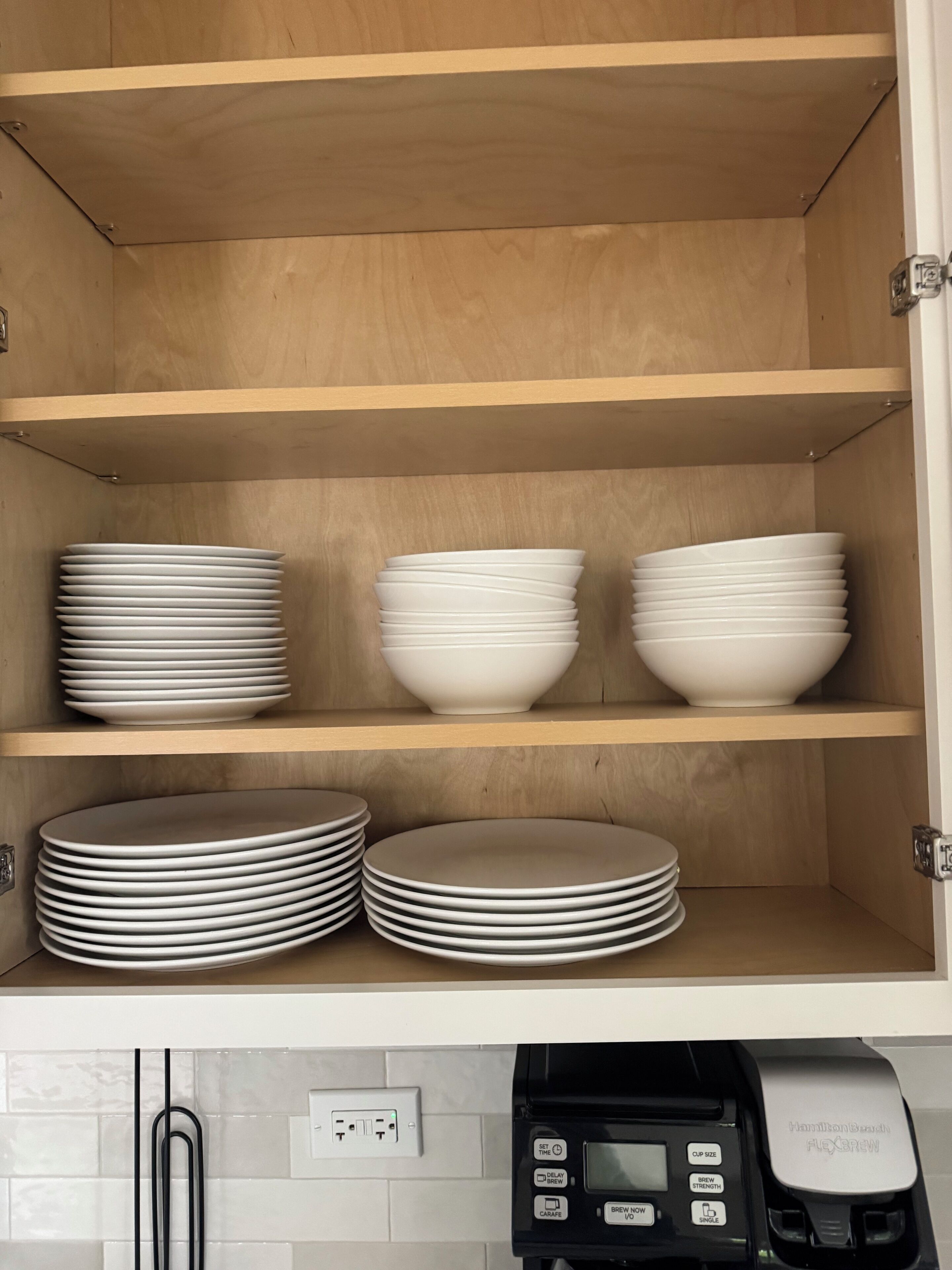 Een keuken met houten planken vol witte borden en kommen.