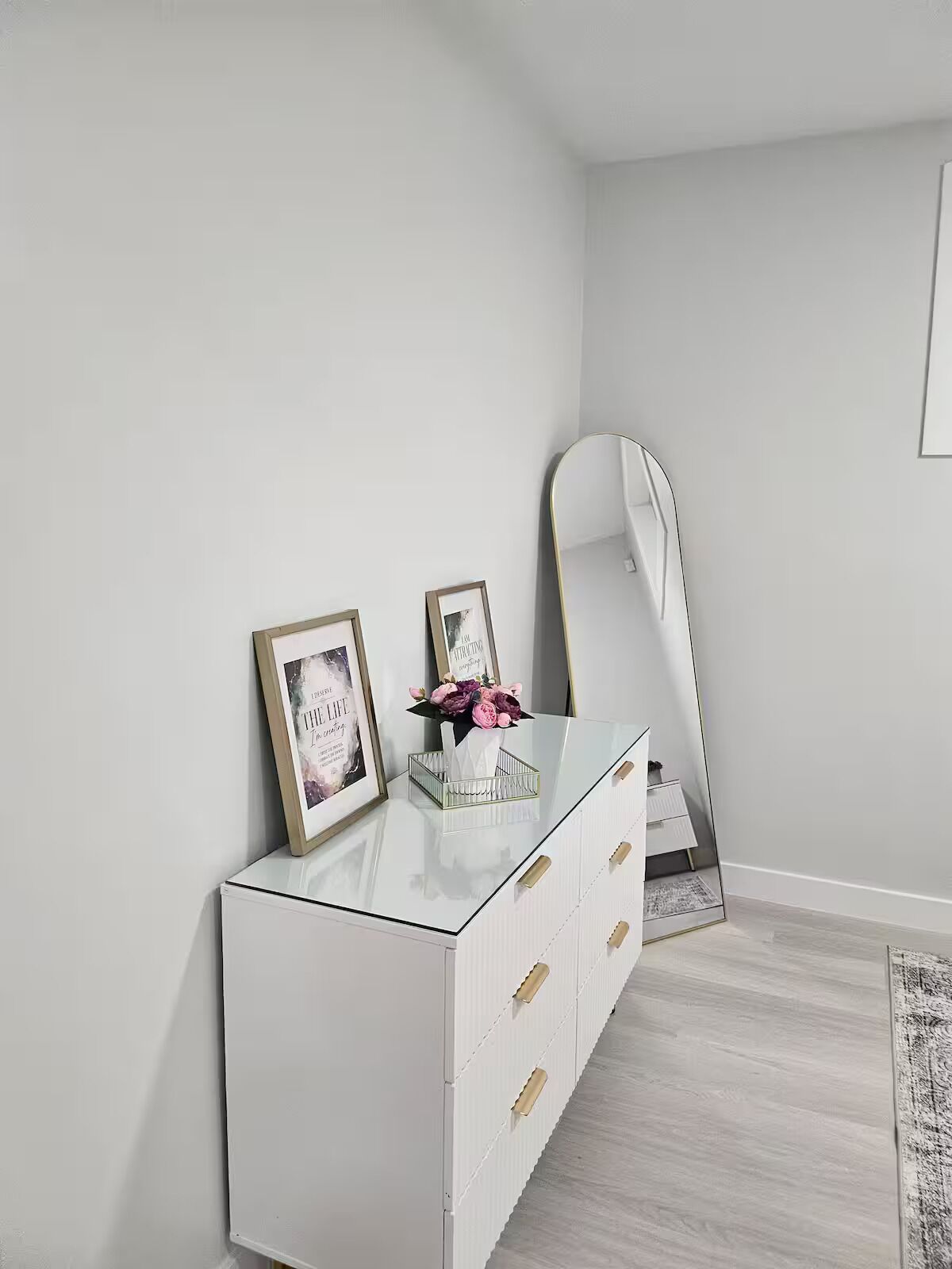 A white dresser with gold handles, a mirror, and two framed pictures.