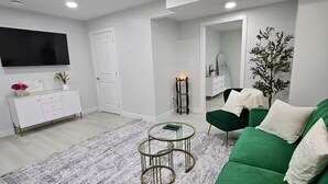 Una sala de estar moderna con un sofá verde, un aparador blanco, un televisor de pantalla plana y una alfombra estampada.