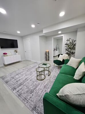 Ein modernes Wohnzimmer mit einem grünen Sofa, einer weißen Kommode, einem Flachbildfernseher und einem gemusterten Teppich.