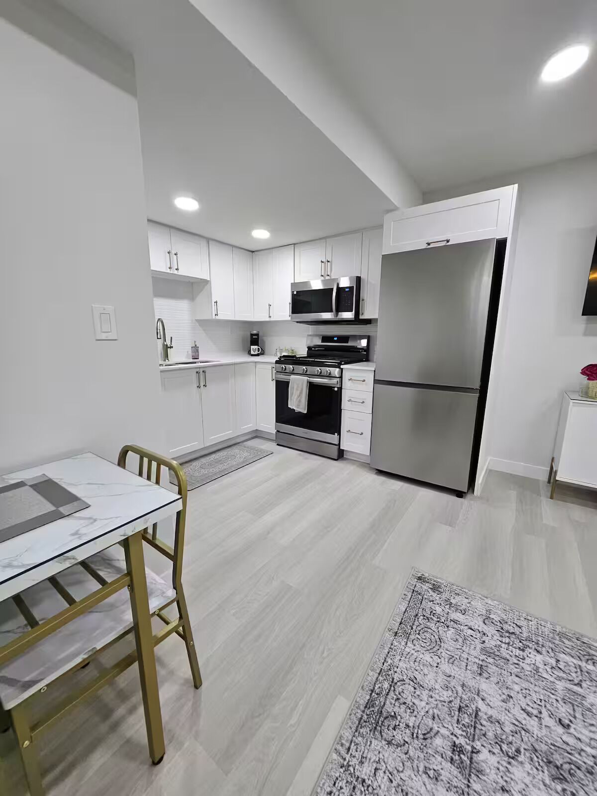A modern kitchen with white cabinetry, stainless steel appliances, and a marble-top dining table.