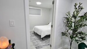 Una habitación con cama, una planta en maceta y una silla con lámpara.