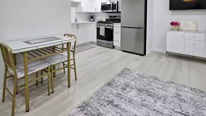 Cocina moderna con gabinetes blancos, electrodomésticos de acero inoxidable y comedor con mesa y sillas de vidrio.