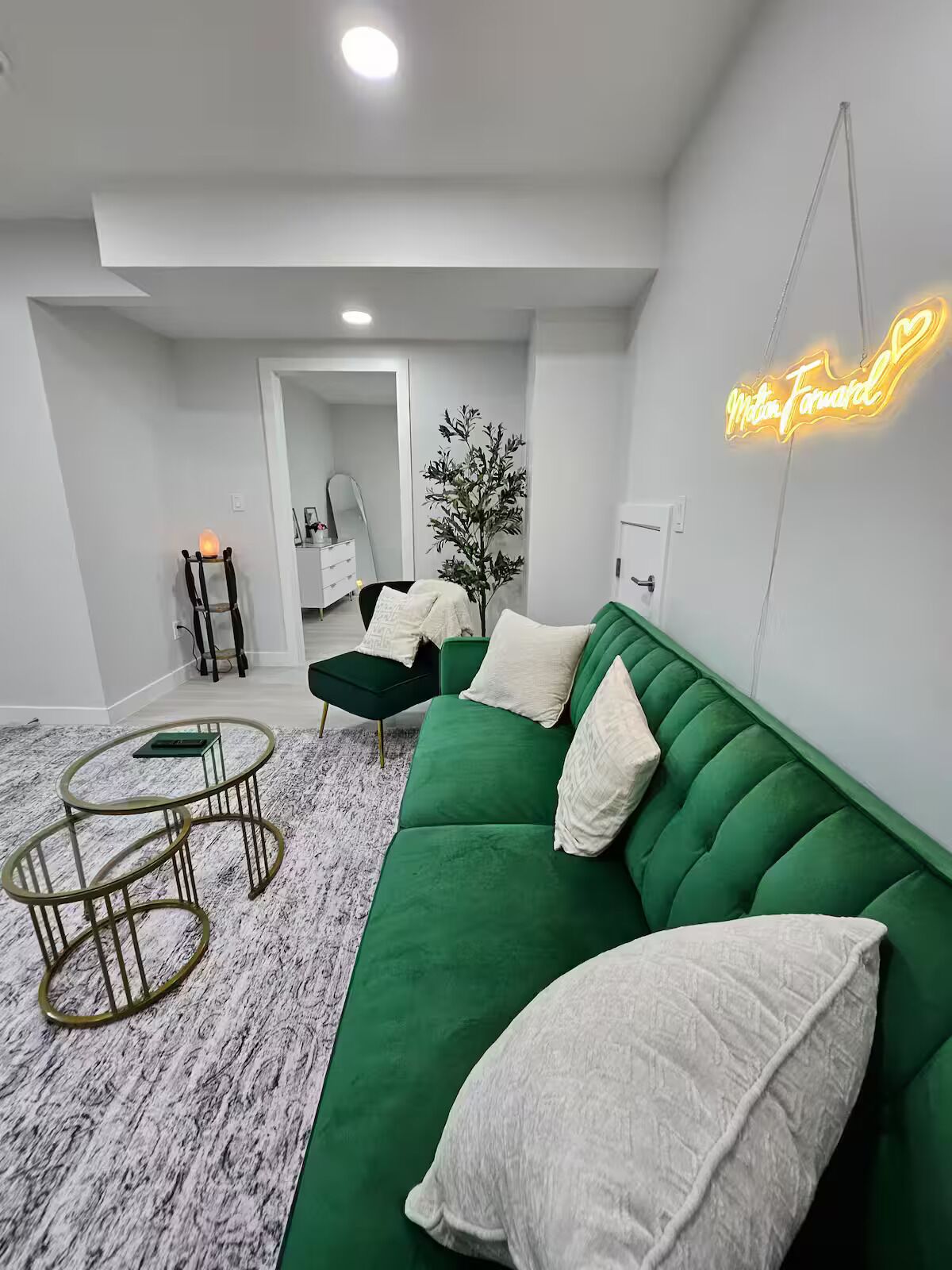 Una sala de estar moderna con un sofá verde, una mesa de centro redonda y un letrero de neón en la pared.