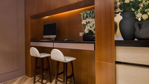 A modern bar area with a wooden accent wall, a flat-screen TV, two white bar stools, and a vase with white flowers. - Yitel Premium (Shanghai)