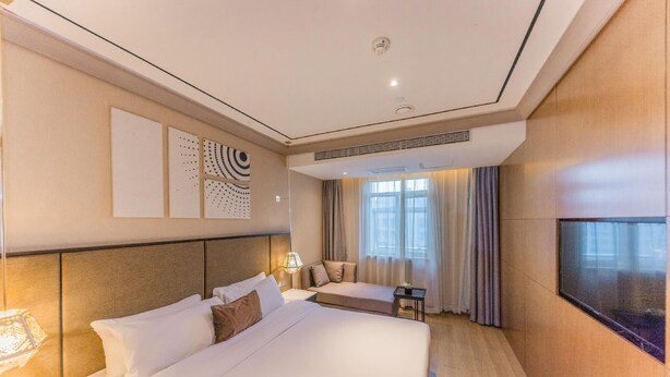 A hotel room with a large bed, a desk, a chair, and a TV mounted on the wall. - Yitel Premium (Shanghai)