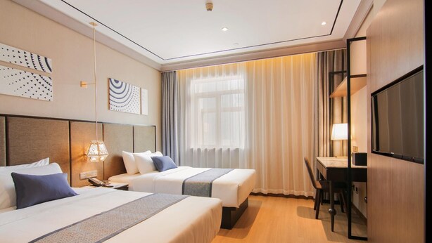 A hotel room with two beds, a desk, a chair, a TV, and a window with curtains. - Yitel Premium (Shanghai)