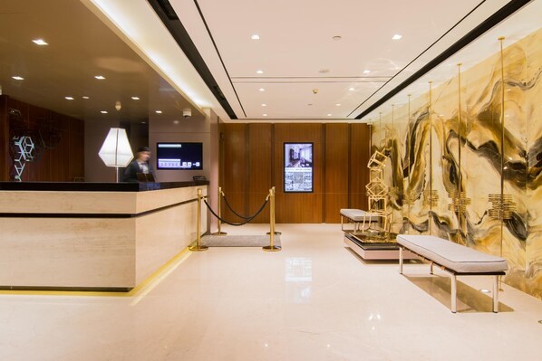 Un espace d’accueil d’hôtel comprenant un comptoir de réception, un écran numérique, un coin salon et un mur décoratif.