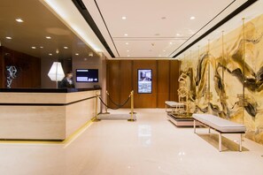 Un espace d’accueil d’hôtel comprenant un comptoir de réception, un écran numérique, un coin salon et un mur décoratif.