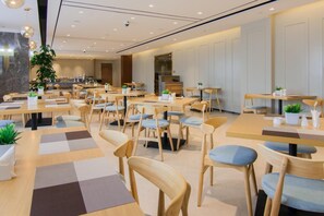 Un espace de restauration moderne, doté de plusieurs tables et chaises, dont certaines sont agrémentées de plantes, et présentant un design épuré et contemporain.