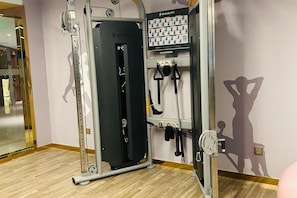 Une salle de sport équipée d’un appareil SHUA, d’une barre de traction et d’un mur orné de silhouettes représentant des exercices.