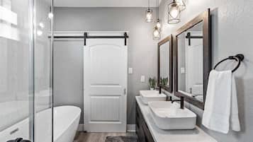 Un baño moderno con cabina de ducha de vidrio, una bañera blanca y un tocador con dos lavamanos.