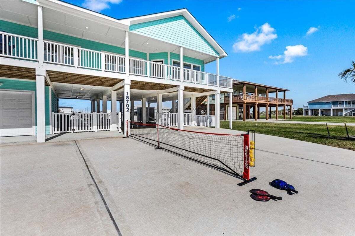 Un edificio de dos pisos con un porche cubierto, cancha de tenis y zona de piscina.