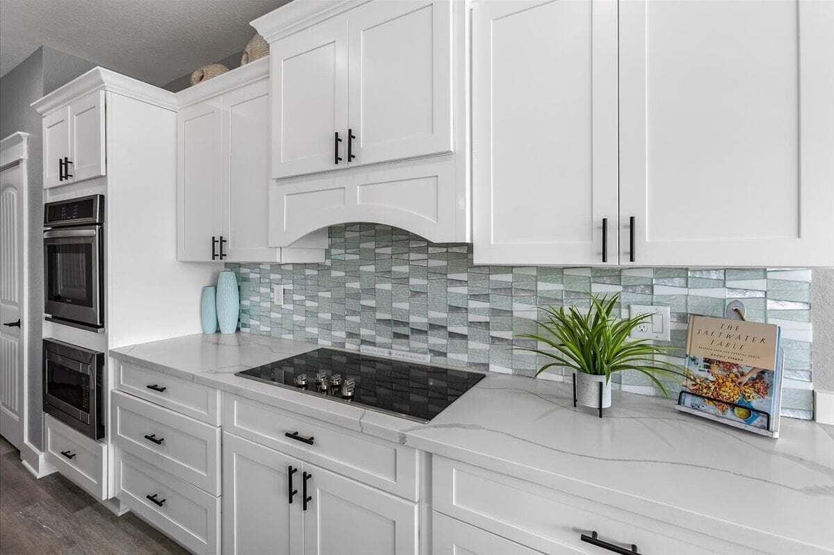 Una cocina moderna con armarios blancos, una estufa negra y un salpicadero de azulejos.