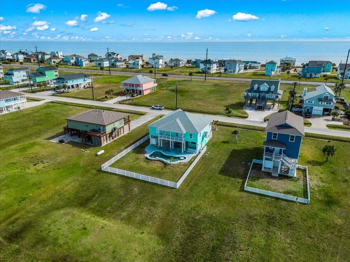An aerial view of a residential area with houses, a swimming pool, and a clear view of the ocean.
