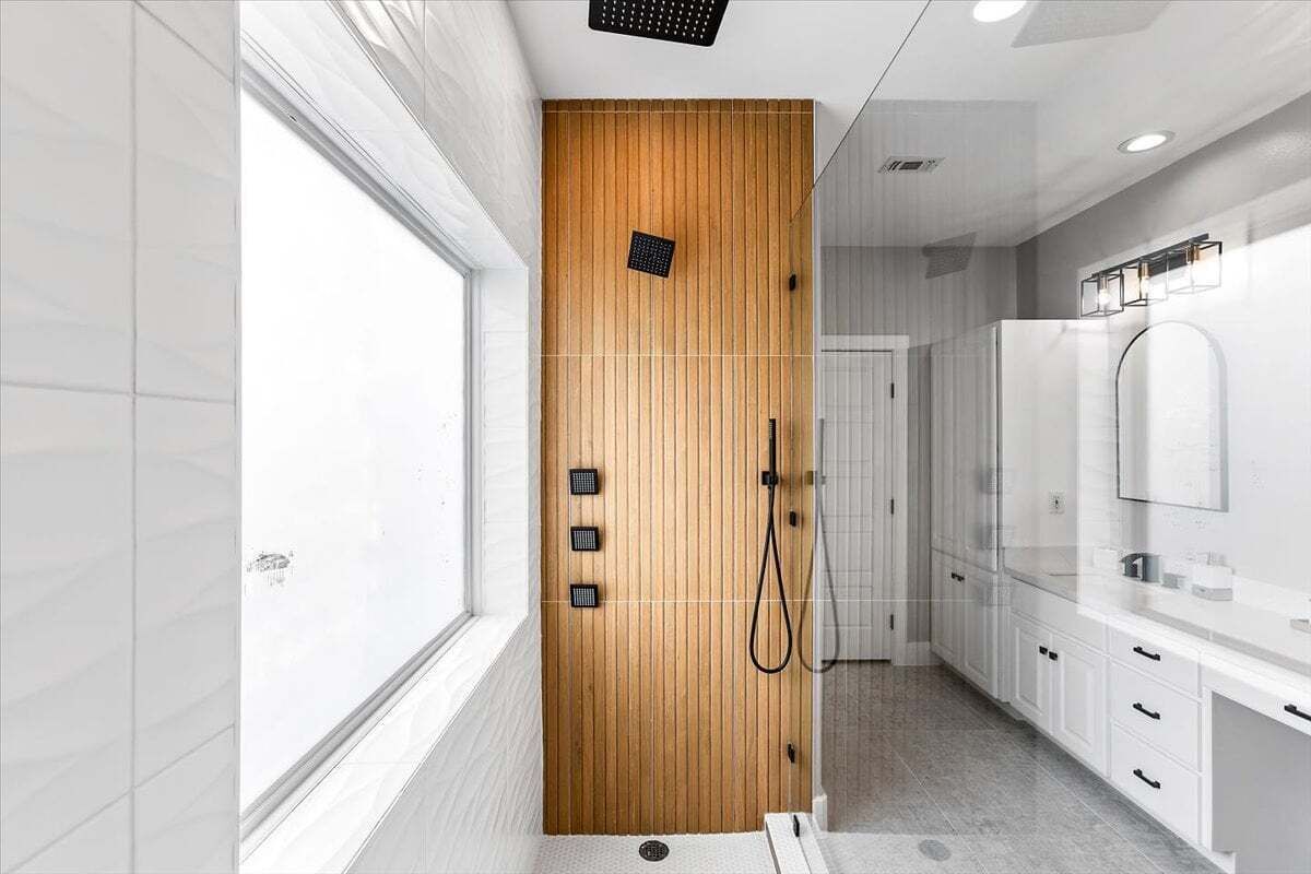 Uma casa de banho moderna com painel de parede de madeira, chuveiro e toucador branco com espelho.