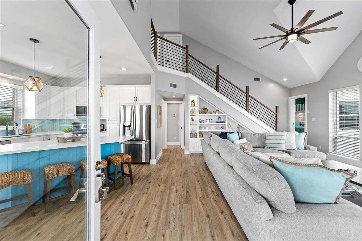A spacious living area with a staircase, a kitchen with a bar, and a large window.