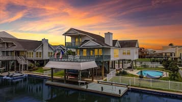 A waterfront property with a pool, a dock, and a house with a balcony.