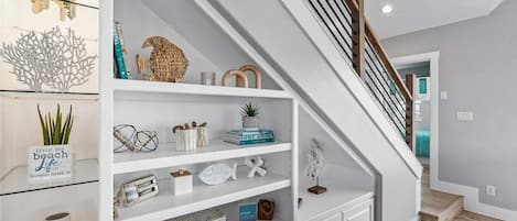 Una escalera con barandillas blancas y un pasamanos de madera que conduce a un rellano con estantes que exhiben varios objetos decorativos.