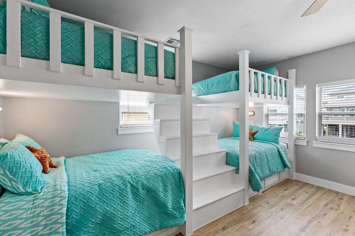 A room with bunk beds, a staircase, and a window with blinds.