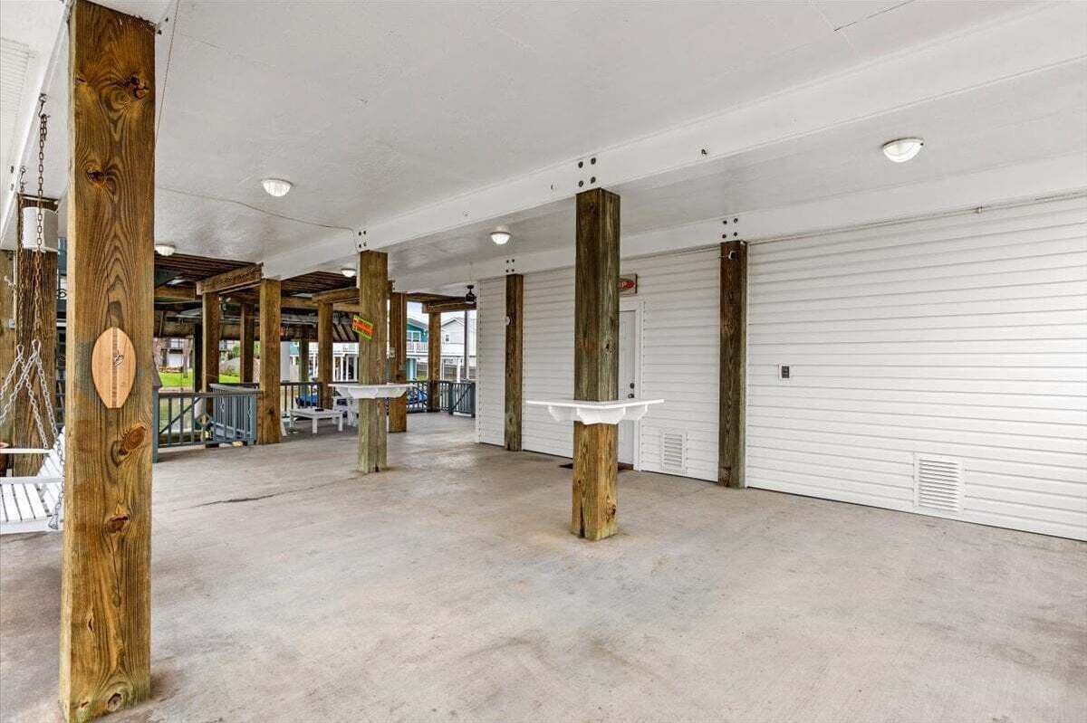 An indoor space with concrete flooring, wooden pillars, and a white garage door.