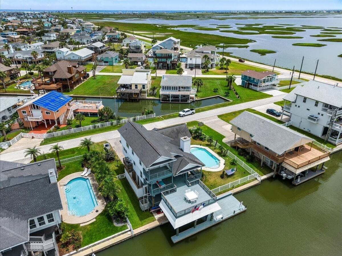 A residential area with houses, a large swimming pool, and a dock extending into a body of water.