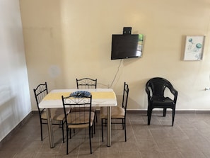 Ein Essbereich mit Tisch und Stühlen, einem an der Wand befestigten Fernseher und einem gerahmten Bild.
