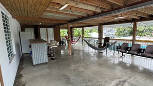 A spacious indoor area with a concrete floor, wooden ceiling beams, a bar area with stools, and a hammock. - 5 suites privadas frente a la playa en Bo Bajos Villa Pesquera Patillas: (Lamboglia)