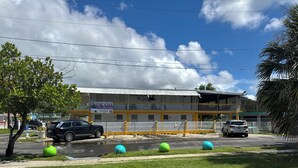 A building with a balcony, a fenced parking area, and a grassy foreground. - 5 suites privadas frente a la playa en Bo Bajos Villa Pesquera Patillas: (Lamboglia)
