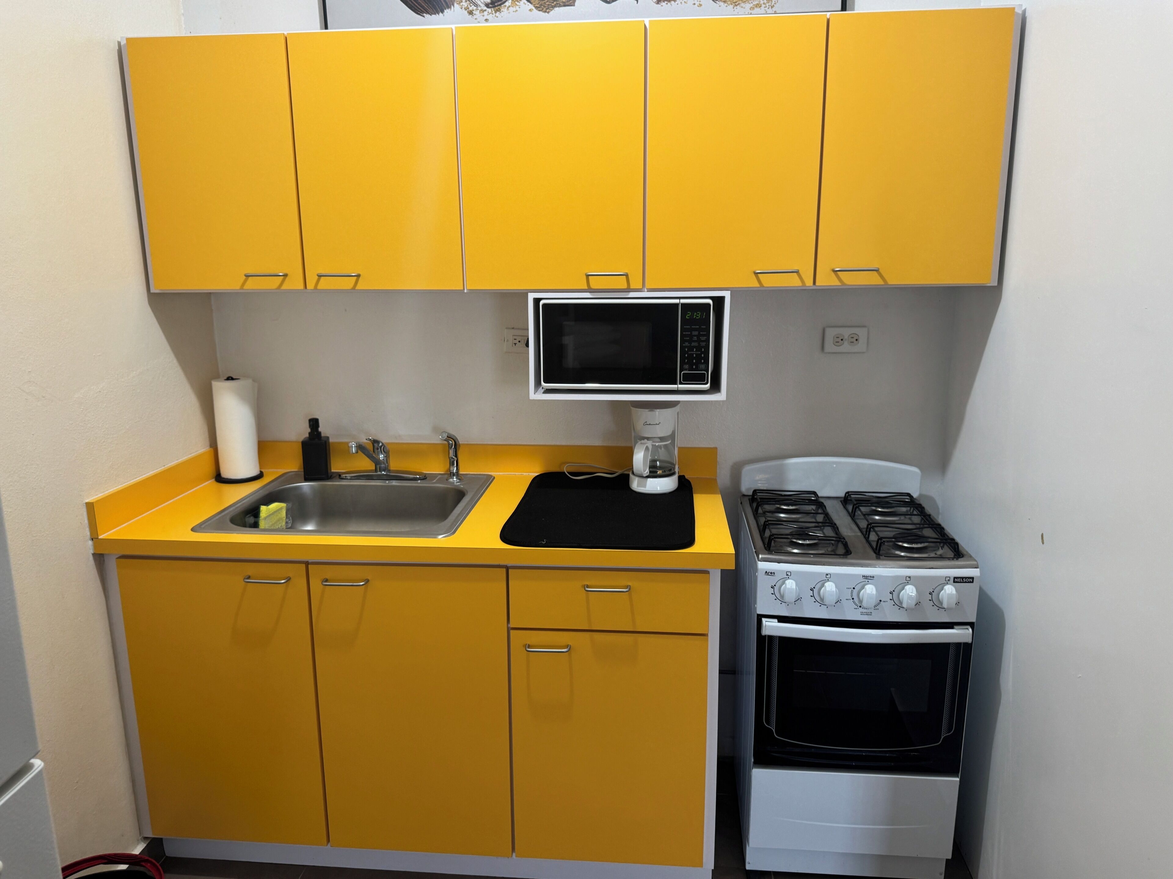 A compact kitchen with yellow cabinets, a microwave, a gas stove, and a sink.