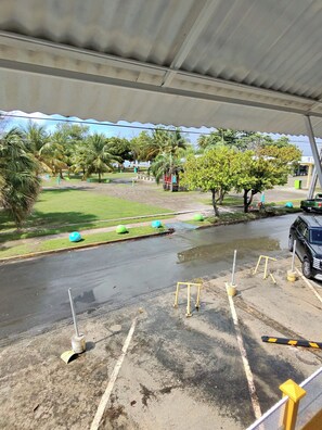 Ein Parkplatz mit überdachtem Bereich, ein grünes Auto und Palmen im Hintergrund.