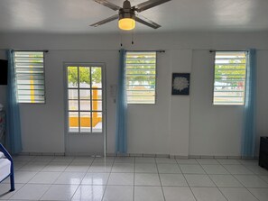Ein Zimmer mit Deckenventilator, einer Tür mit Blick und Fenstern mit Vorhängen.