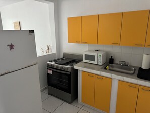 Eine Küche mit Gasherd, Backofen, Mikrowelle und gelben Schränken.