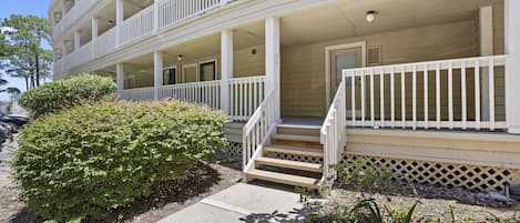 A multi-story building with a porch, steps, and a small garden area.
