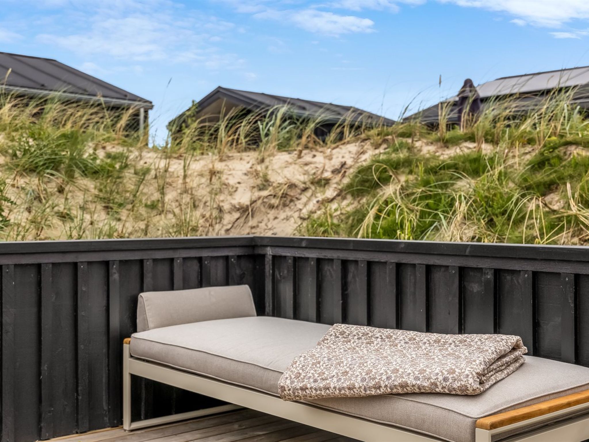 Un lit installé sur la plage, avec vue sur les dunes et les cabanes de plage.