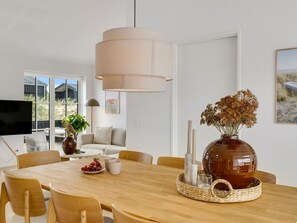 Ein moderner Essbereich mit Holztisch, Stühlen, einer Vase mit Trockenblumen und einer großen Pendelleuchte.