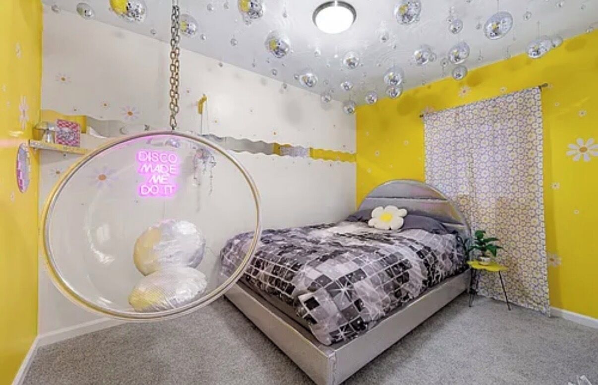 A bedroom with a bed, a hanging chair, a wall with a floral pattern, and a ceiling with bubbles.