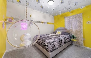 Ett sovrum med en säng, en hängstol, en vägg med ett blommönster och ett tak med bubblor.