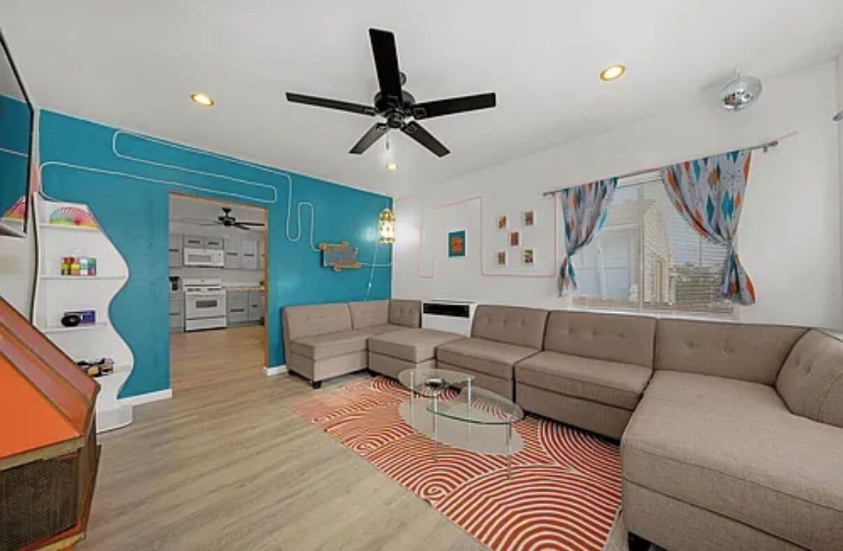 A modern living room with a sectional sofa, a glass coffee table, and a ceiling fan.