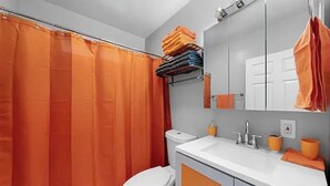 A bathroom with a white toilet, an orange shower curtain, and a sink with a mirror above it. - North Park 3BR Furnished Rental—31-Night Minimum (San Diego)