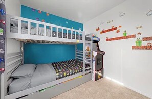 Ein Schlafzimmer mit Etagenbetten, einer blauen Wand und einer Wanddekoration zum Thema Mario, sowie eine Nintendo 64 Konsole.