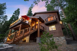 A wooden cabin with a balcony, stone foundation, and string lights. - Brand New Kings Beach Retreat  Lake Views + Forest (Kings Beach)